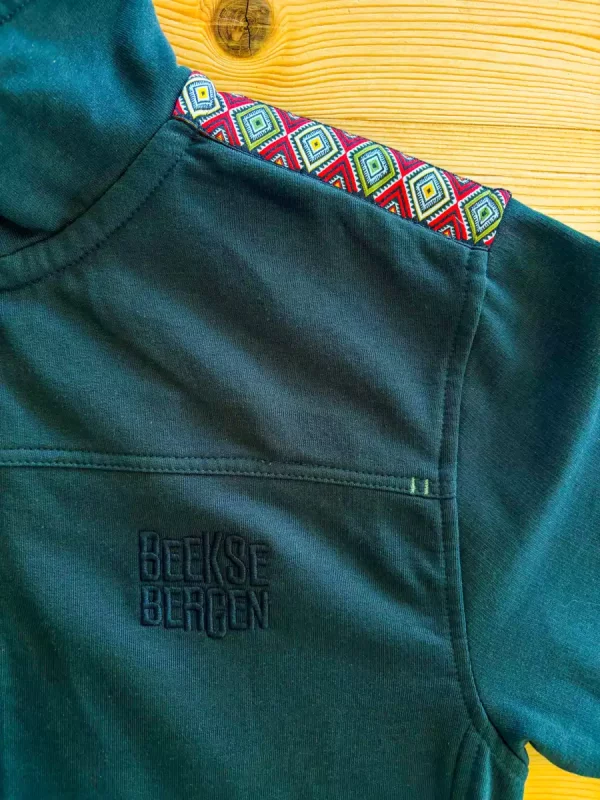 Detail van een groen shirt met geborduurd patroon op de schouder