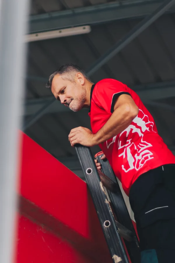 Medewerker van De Romein in rode werkkleding klimt op een machine