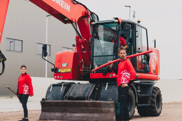Medewerkers van De Romein in rode werkkleding bij een graafmachine