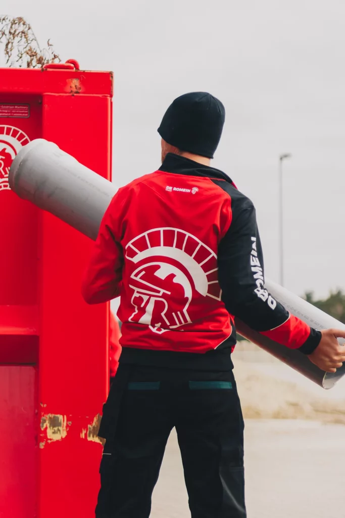 Medewerker van De Romein in rode werkjas met logo op de rug