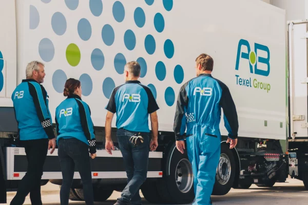 Medewerkers van AB Texel in bedrijfskleding lopen langs een truck
