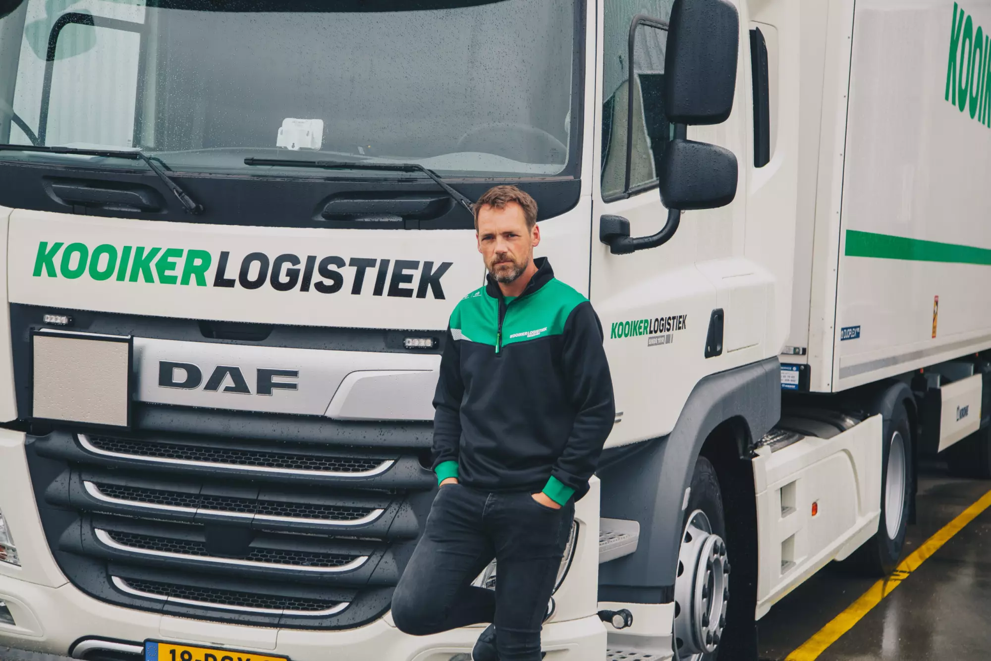 Chauffeur van Kooiker Logistiek in bedrijfskleding voor een DAF-truck