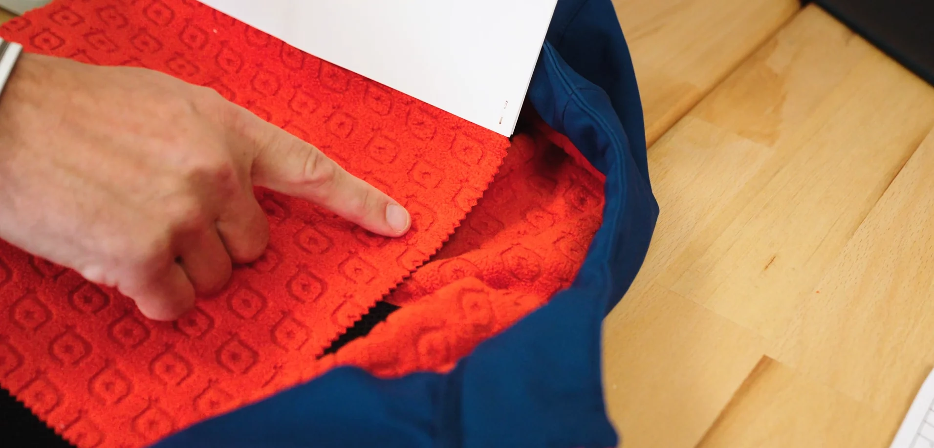 Een hand wijst een rode stofstaal aan naast een blauwe werkjas
