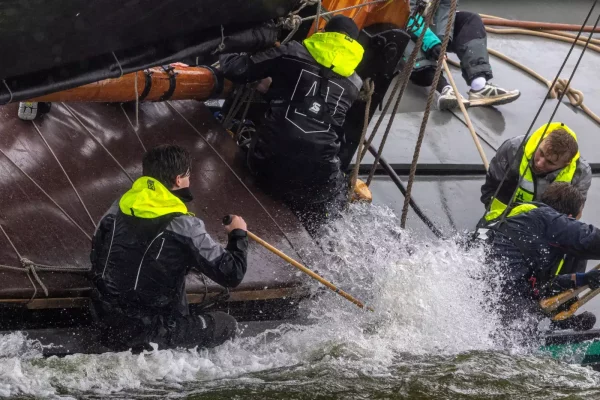 Bemanning van De Sneker Pan in zeilkleding tussen de golven
