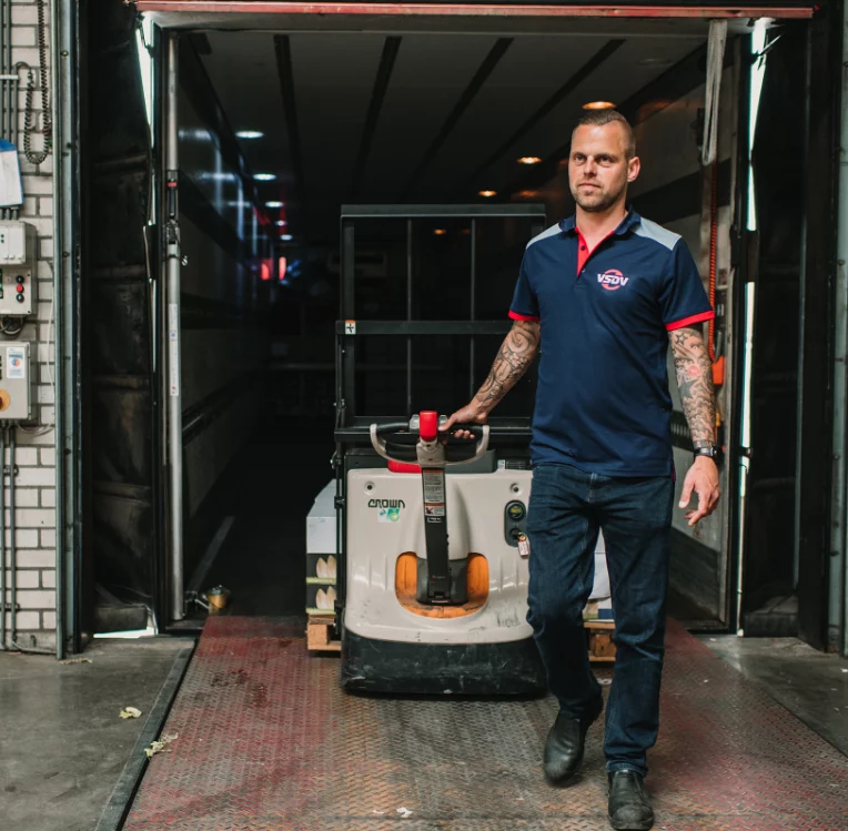 Medewerker in bedrijfskleding met een pallettruck in de laadbak van een vrachtwagen